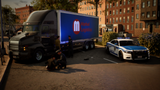 A large semi-truck with a blue side panel reading Madrid Logística is parked in an urban lot alongside a white and blue police car. Several people are gathered around the truck, and brick buildings, trees, and pavement are visible in the background.