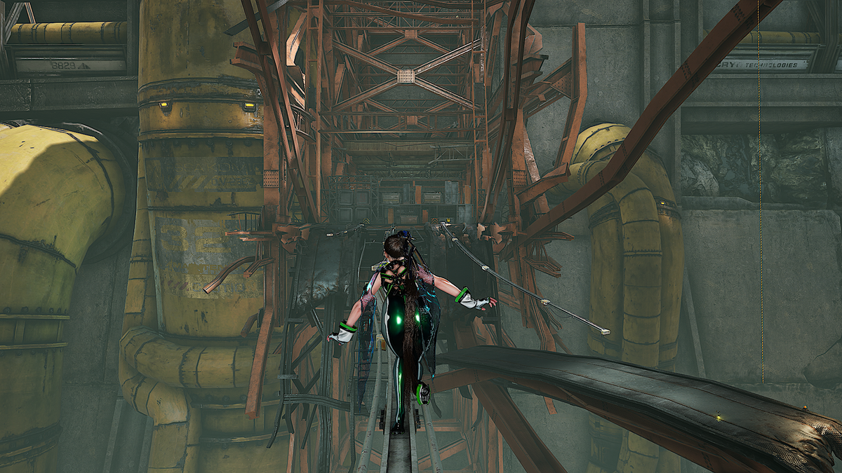 A video game scene showing a female character with glowing green eyes and dark hair standing on a narrow walkway in a large industrial interior with pipes, metal beams, and yellow machinery.